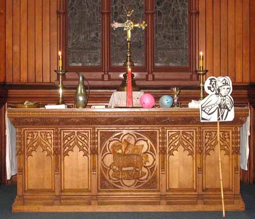 Wooden altar, bearing a large cross and two candles. There are several objects on the altar, and the St Augustine's emblem is displayed at the right-hand side.
